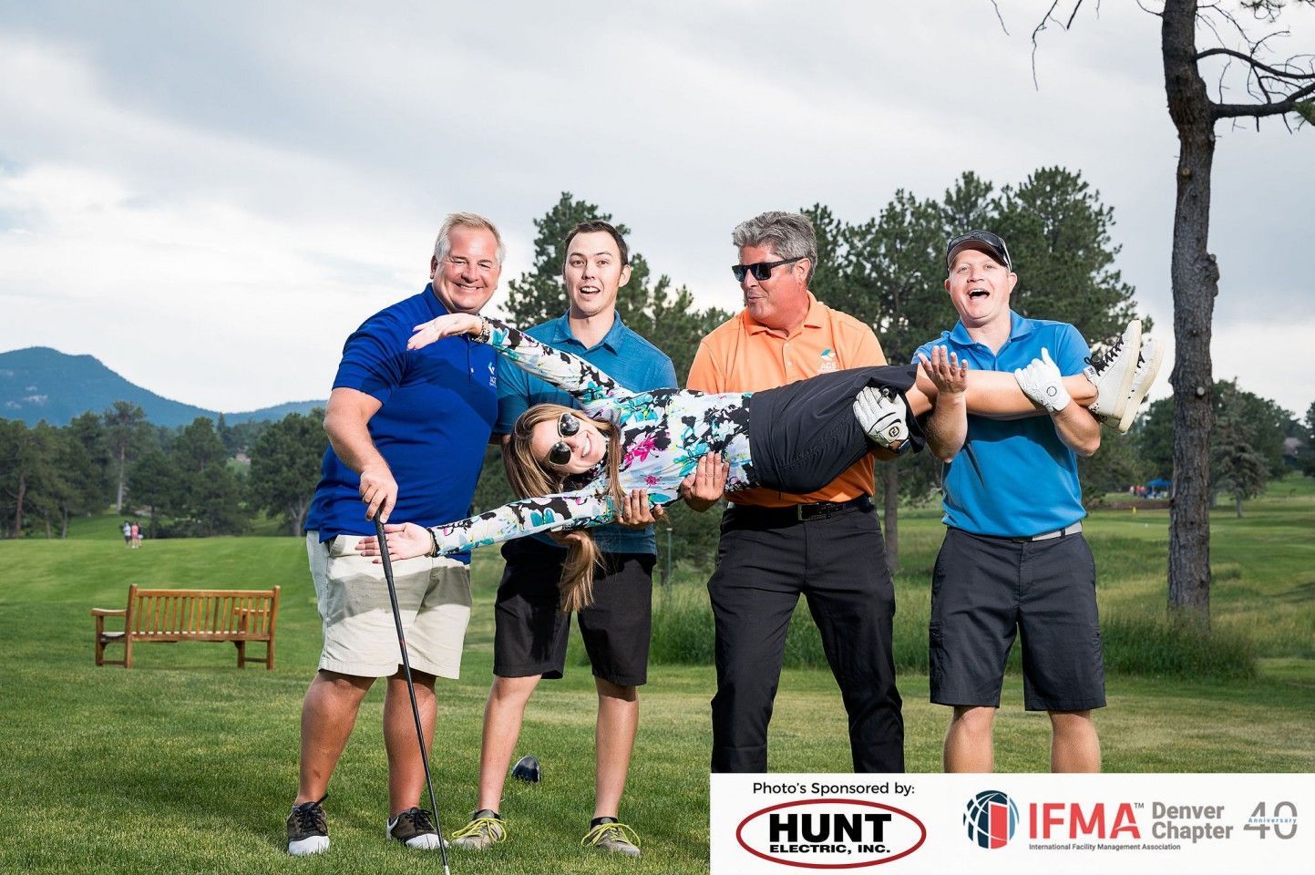 Four people holding a person horizontally on a golf course, laughing.