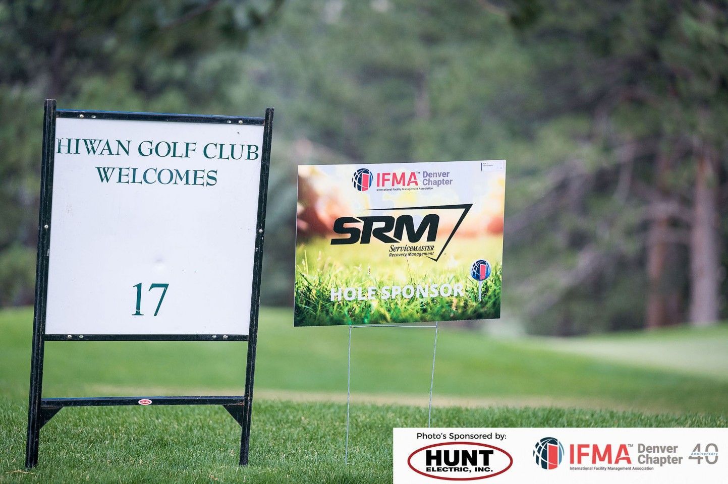 Two golf course signs: one welcomes to Hiwan Golf Club, the other advertises SRM 7. Green grass setting.