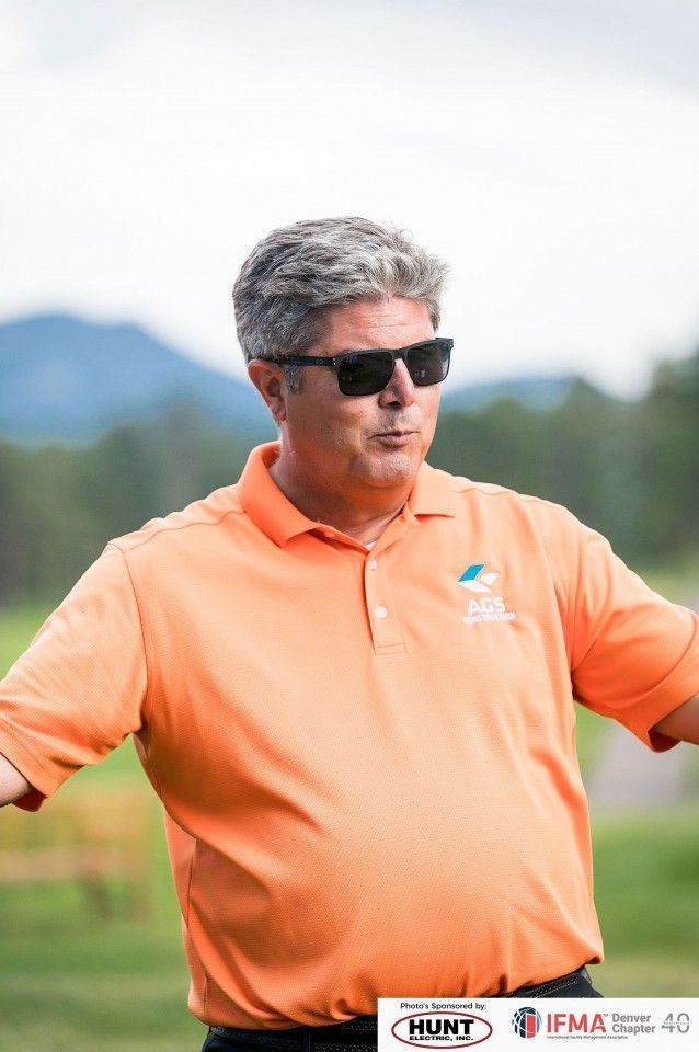 Man in orange polo shirt and sunglasses, arms outstretched, outside.
