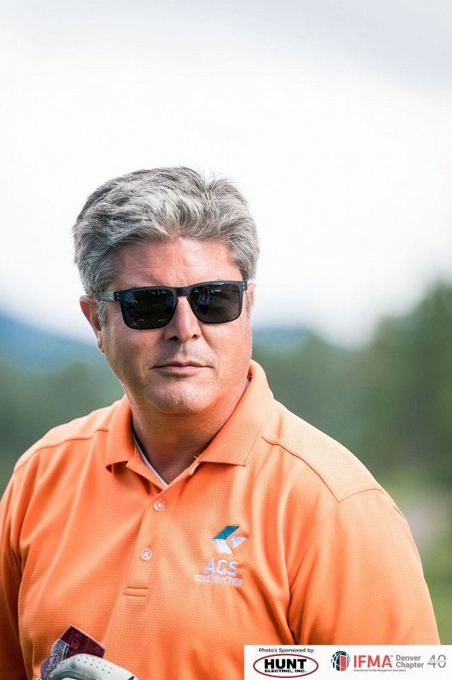 Man wearing sunglasses and orange polo shirt, looking to the side outdoors.