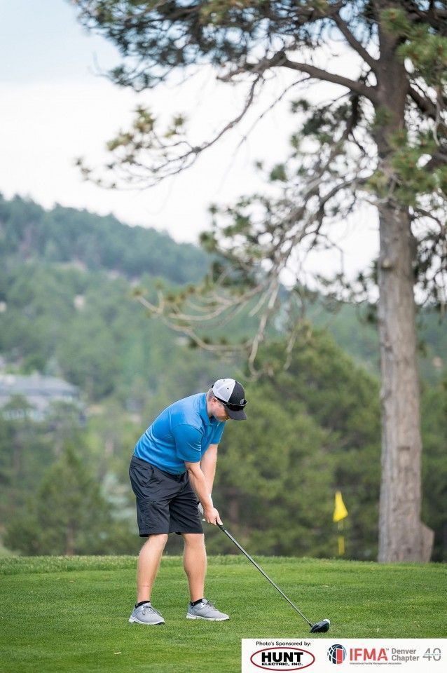 Golfer tees up on a green, mountain backdrop, overcast sky.