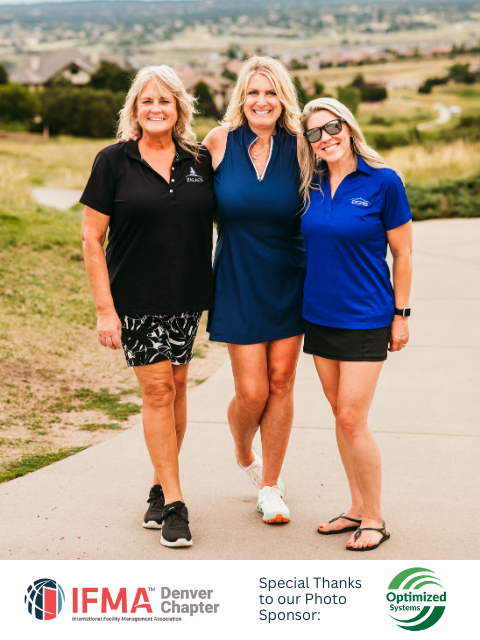 Three women smiling, posing on a golf course. One in a blue dress, the others in black and blue shirts, shorts.