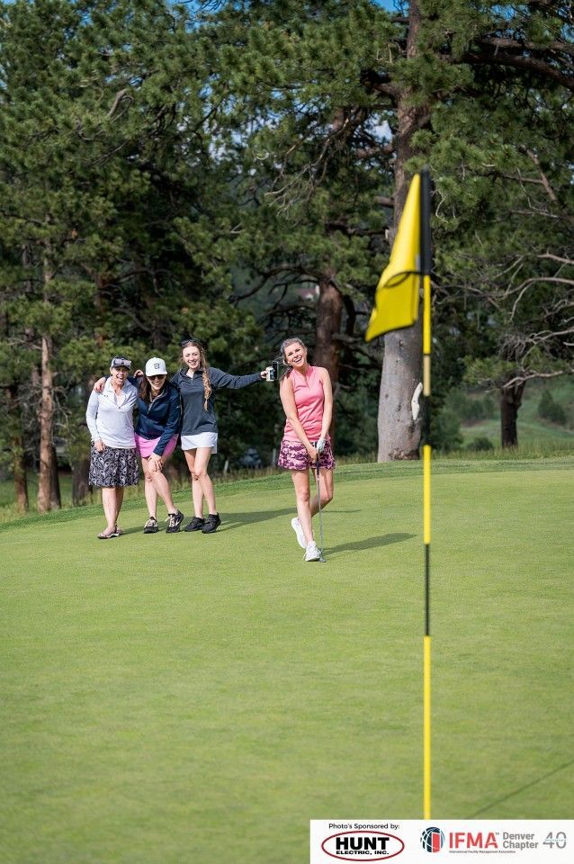 Golfer swings near the yellow flag, friends watch on green golf course.