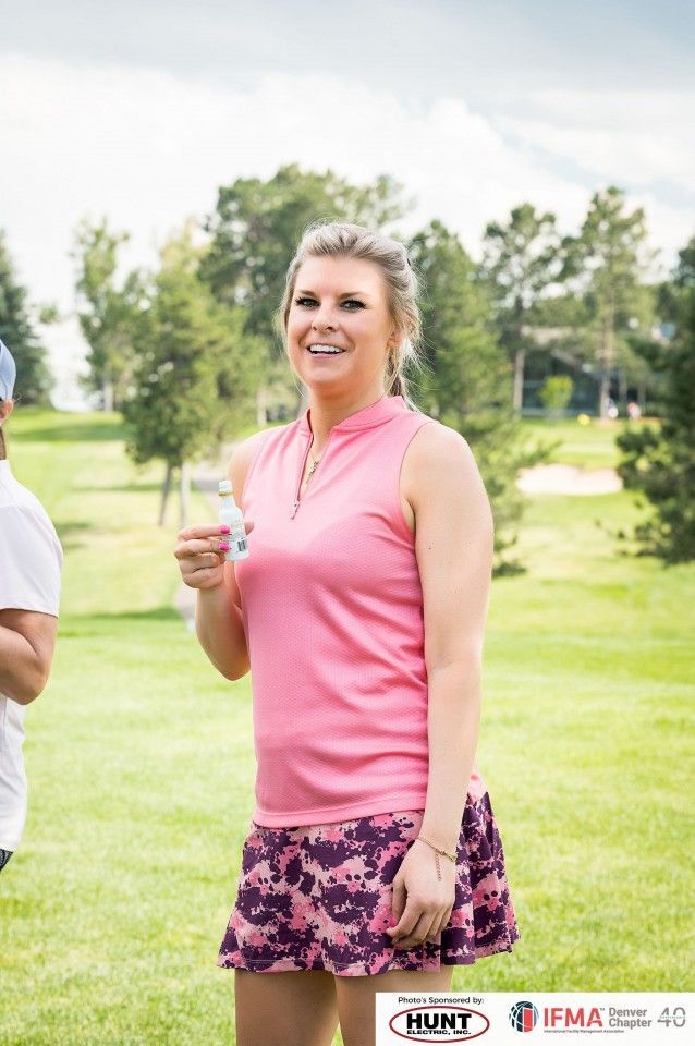 Woman in pink golf attire smiling outdoors, holding small object.