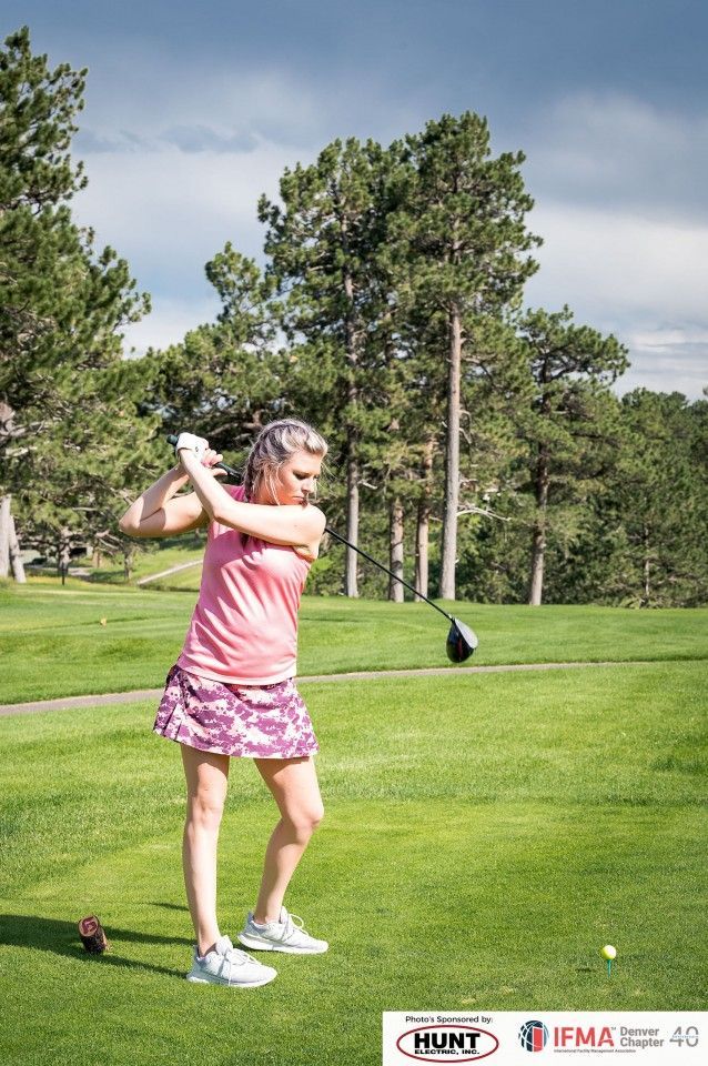 Woman in pink golf attire swings a club on a green course.