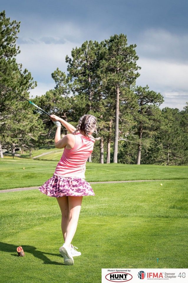 Woman in pink golfing on a green course, swinging club.