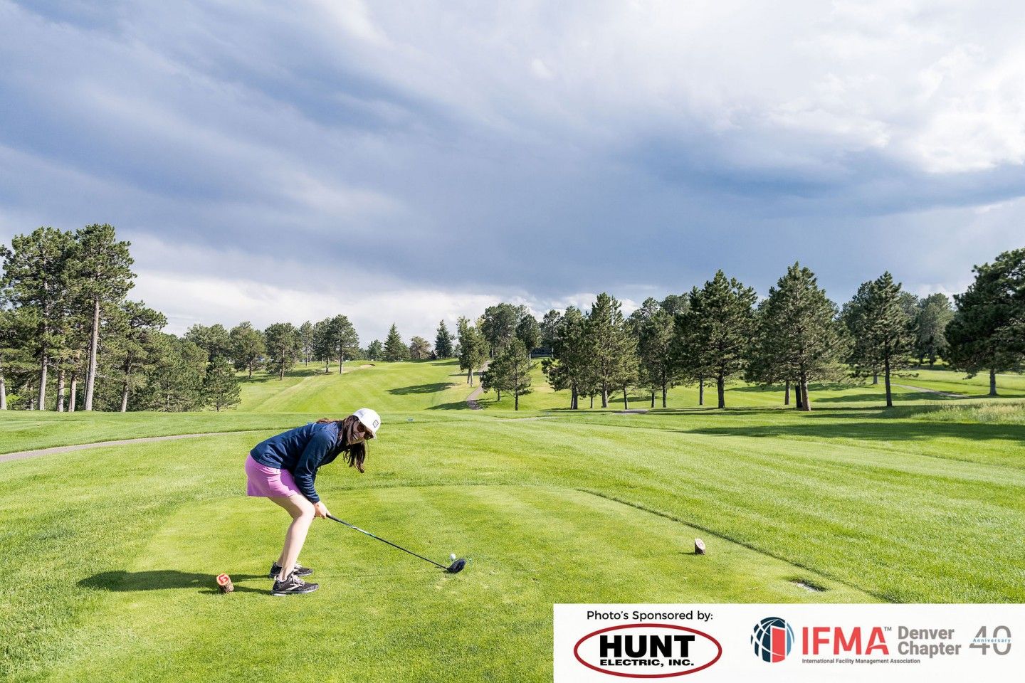Woman teeing off on a green golf course under a cloudy sky.