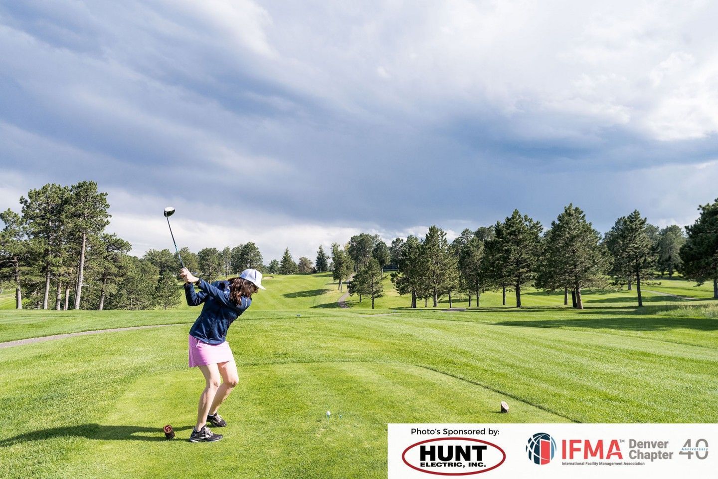 Golfer swinging club on a green course under a cloudy sky.