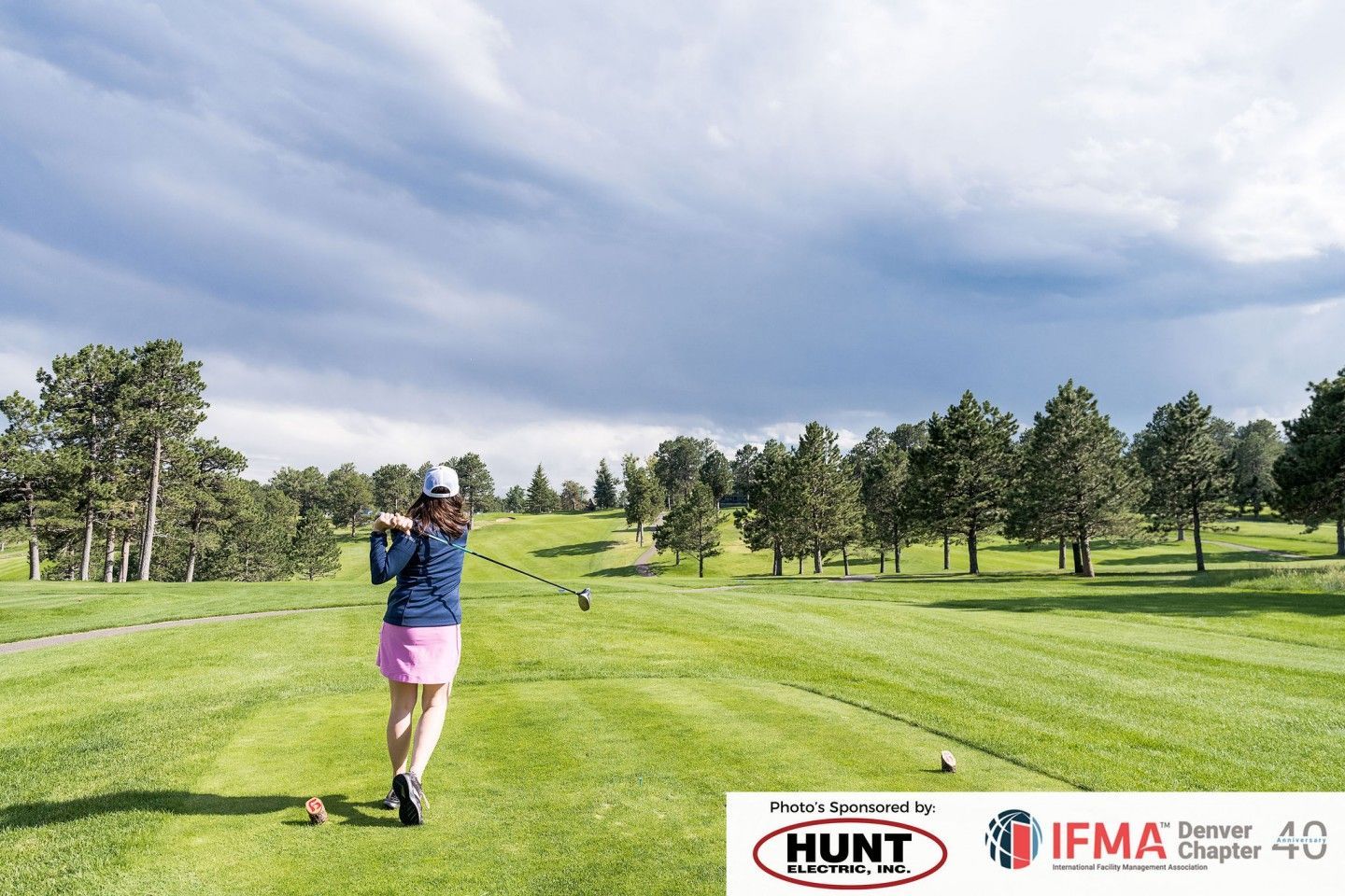 Woman swinging a golf club on a green course under a cloudy sky.