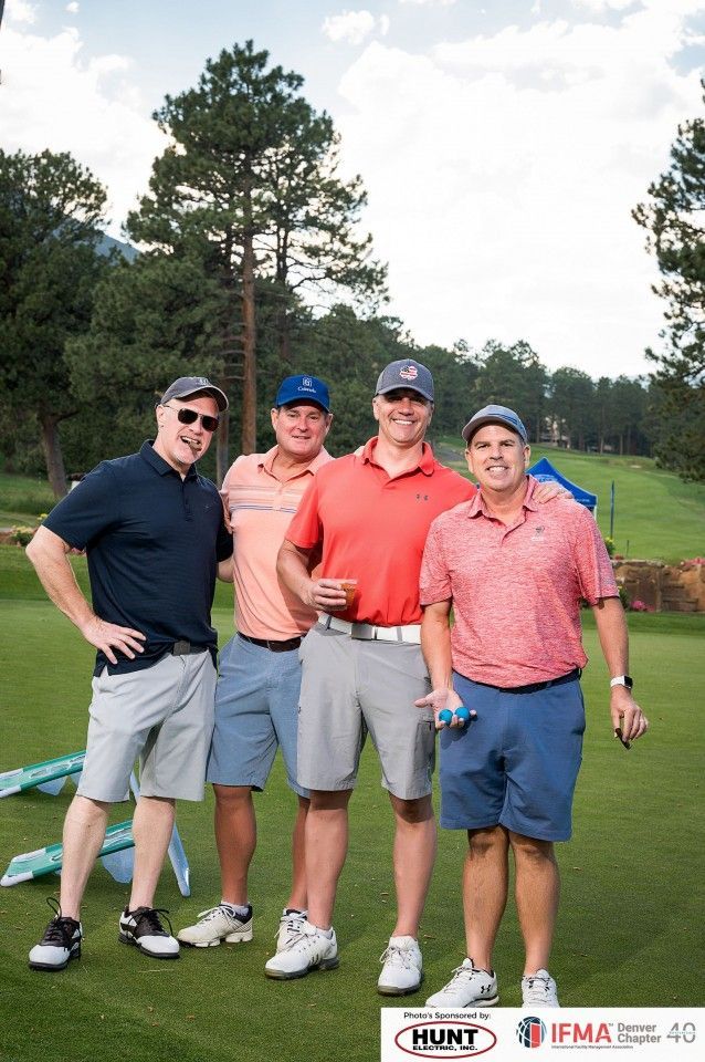 Four men in golf attire pose on a golf course.