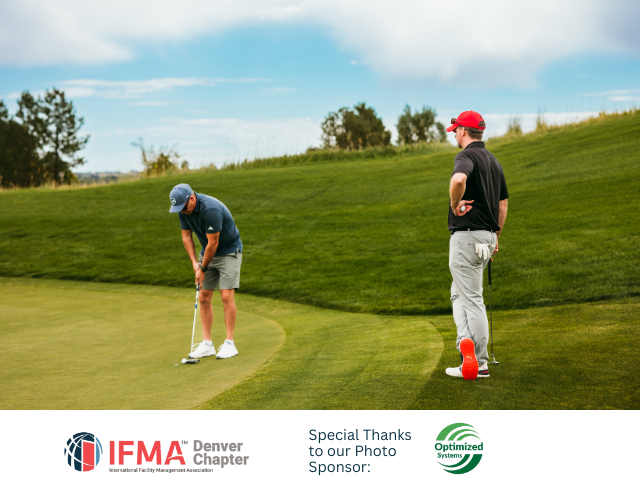 Two golfers on a green: one puts a golf ball, another watches near a red marker.