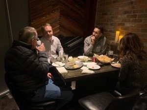 Four people seated around a table in a dimly lit restaurant. Food and drinks are present.