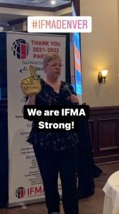 Woman speaking at an event, holding a foam finger.  