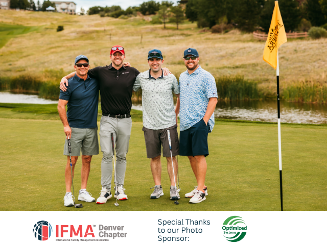 Four men on a golf course pose near a flag. They are wearing golf attire, arms around each other, smiling.