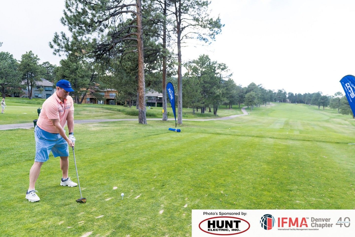 Man in blue hat and shorts swings golf club on a green course.