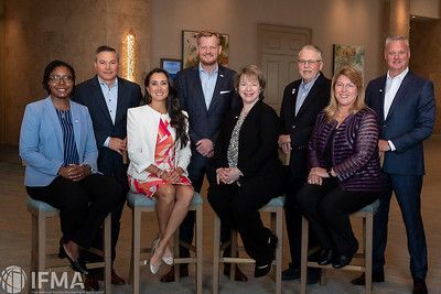 Group of nine people in business attire posing for a photograph in a well-lit interior.