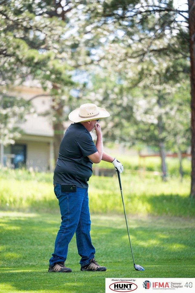 Person in jeans and hat on a golf course, holding a club, touching face.