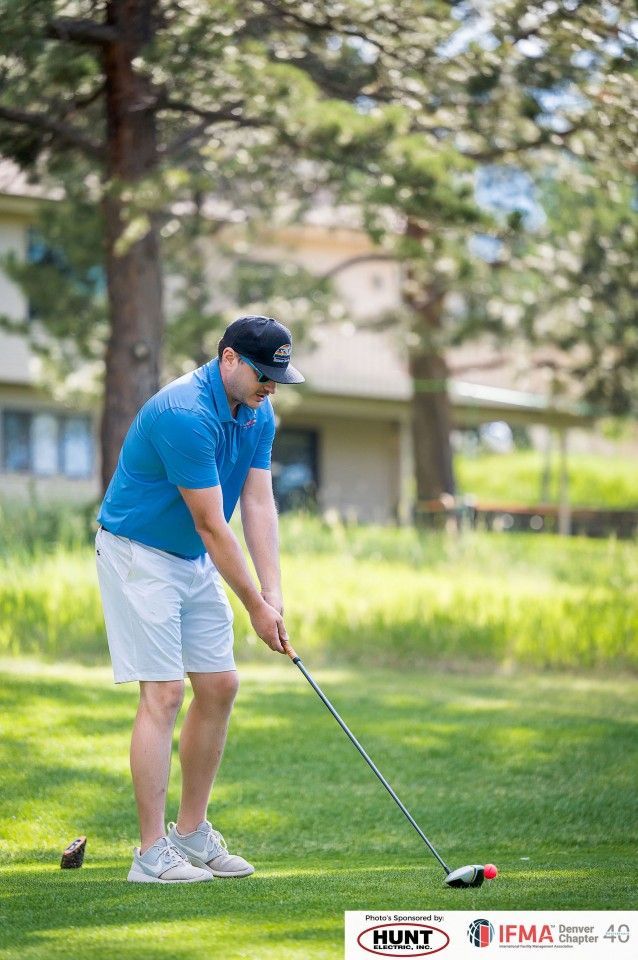 Man in blue shirt and white shorts golfing outdoors, swinging club.