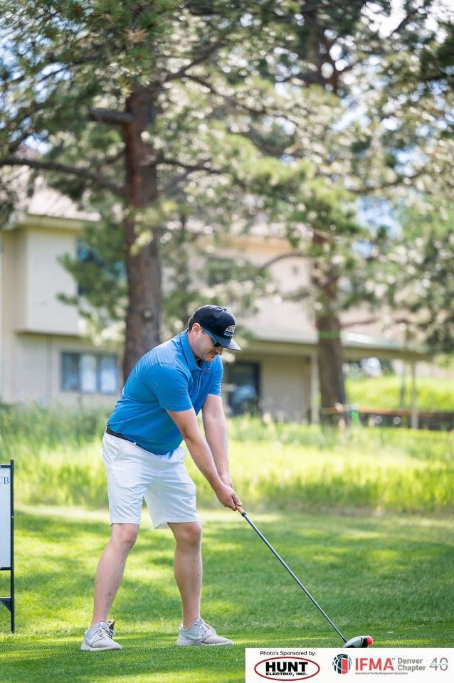 Man in blue shirt and white shorts golfing outdoors, teeing off on green grass.