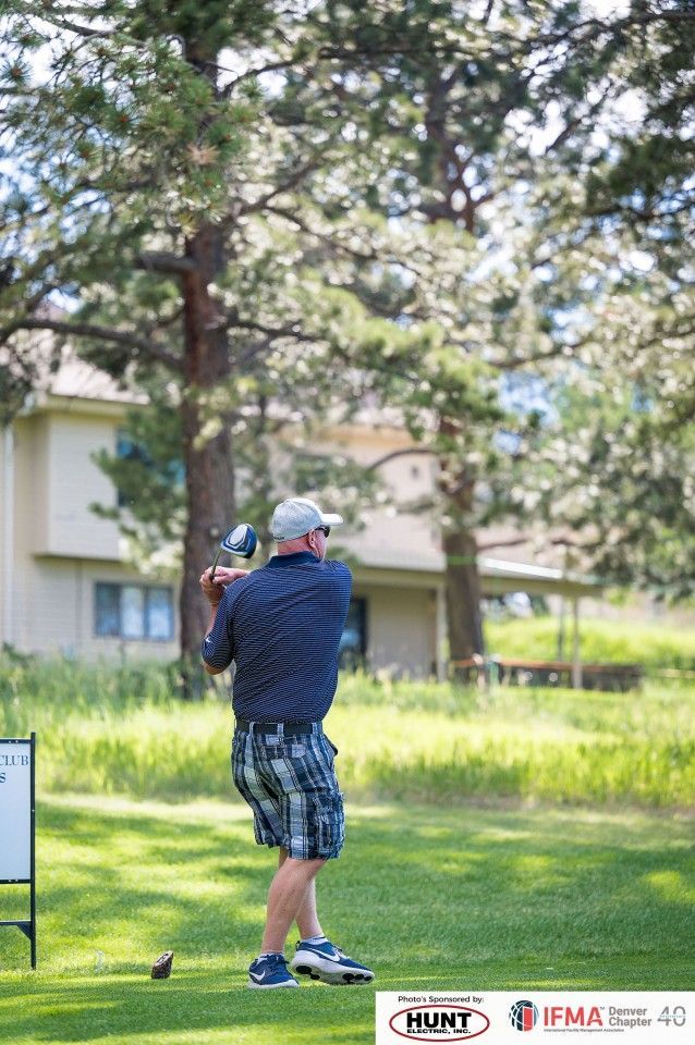 Golfer swinging club on a golf course, wearing plaid shorts and a blue shirt.