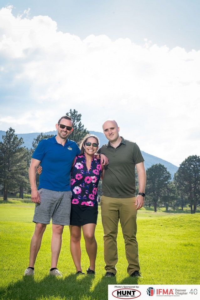 Three people standing on a green field under a cloudy sky