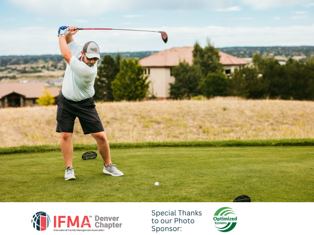 Man swinging a golf club on a green, with golf ball in front. Houses and hills in the background.