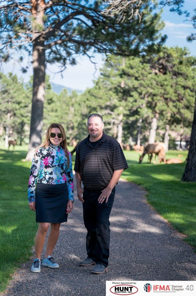 Woman in floral shirt and man in black shirt stand on a path. Golf course setting, sunny day.
