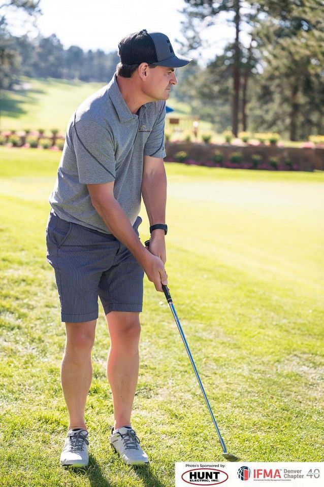 Man wearing golf attire, lining up a golf shot on a sunny course, holding a club.