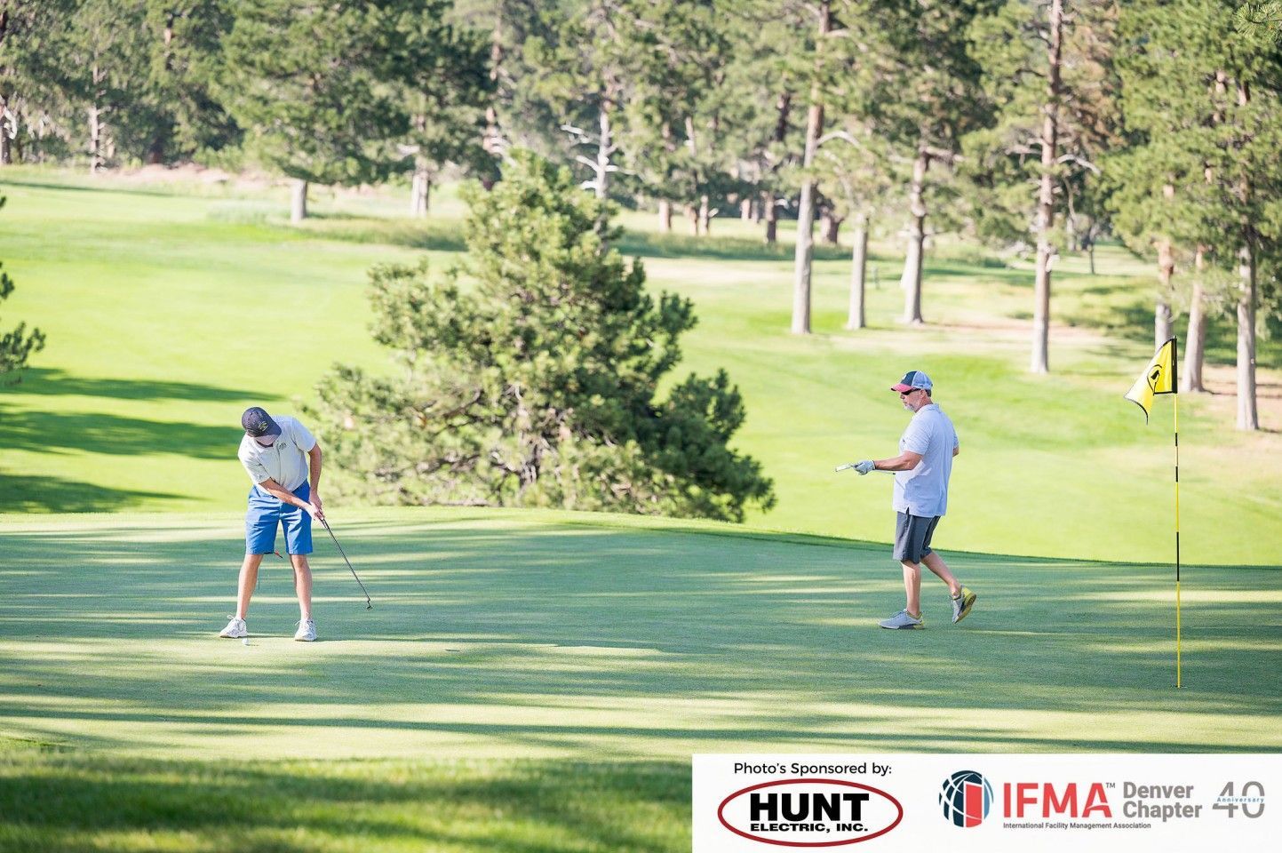 Two golfers on a green: one putting, the other watching. Golf course setting, sunny day.