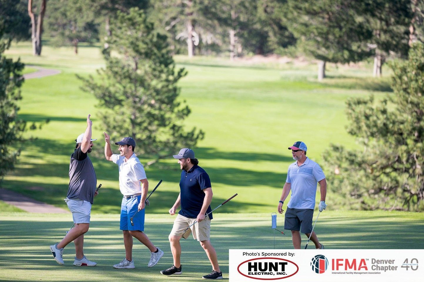 Four golfers on a green celebrate. Two high-five while others watch, sunny day.