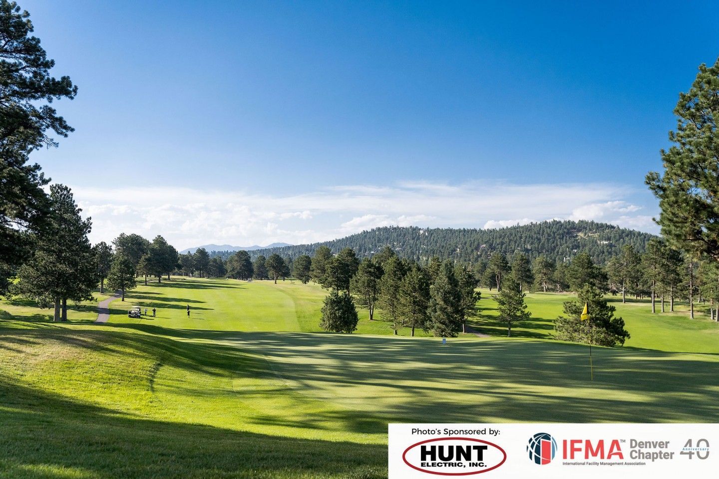 Green golf course with trees under a blue sky. Mountains in the background. Sponsored by Hunt and IFMA.