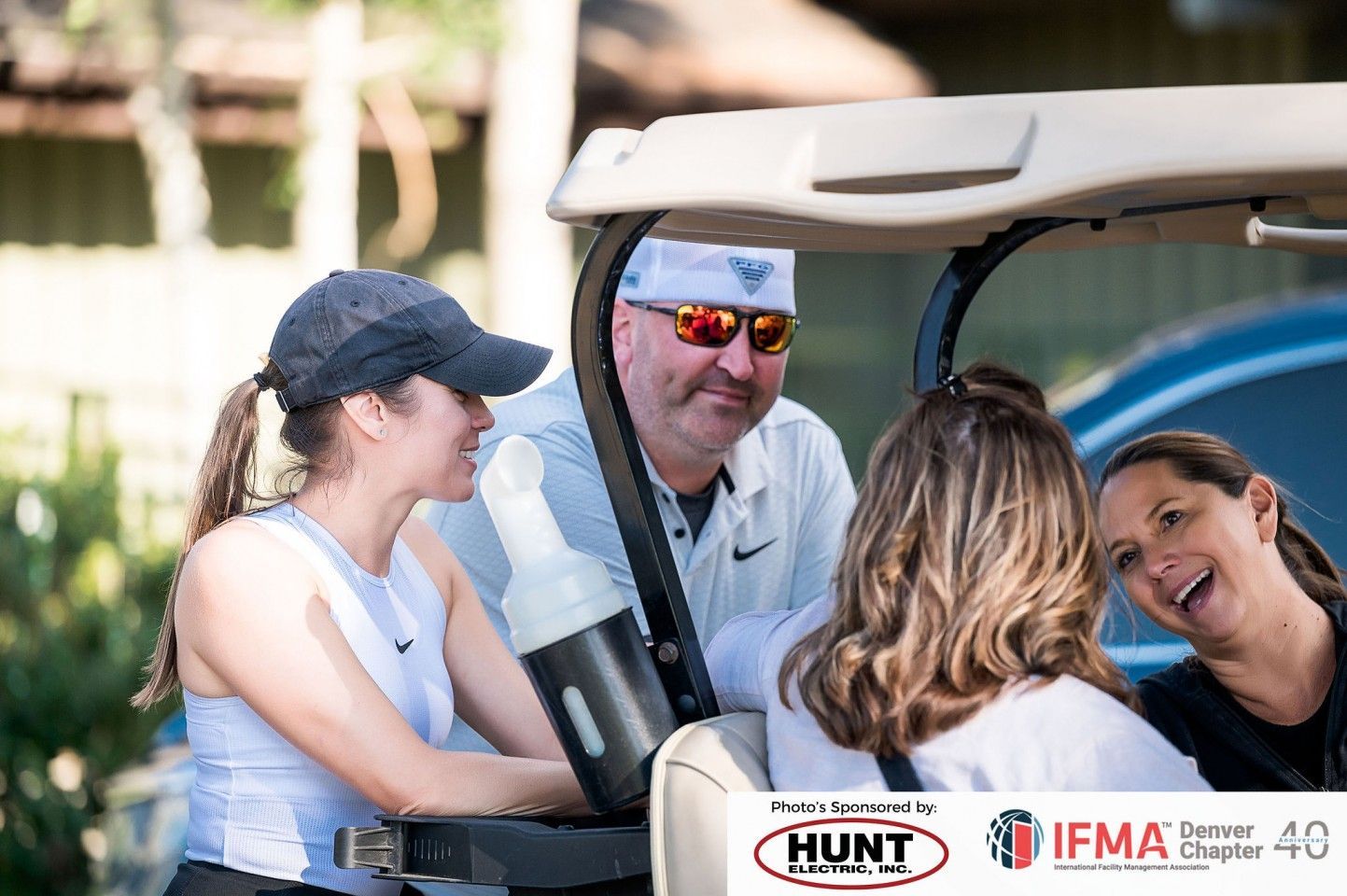 Four people around a golf cart, smiling and talking outdoors.