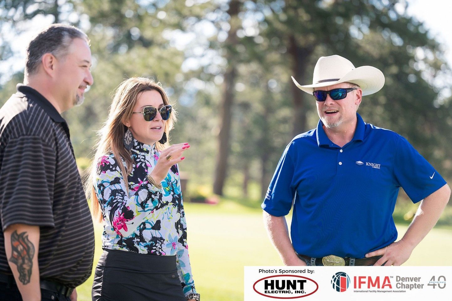 Three people on a golf course: woman blowing a kiss, man in cowboy hat smiling, man in striped shirt.