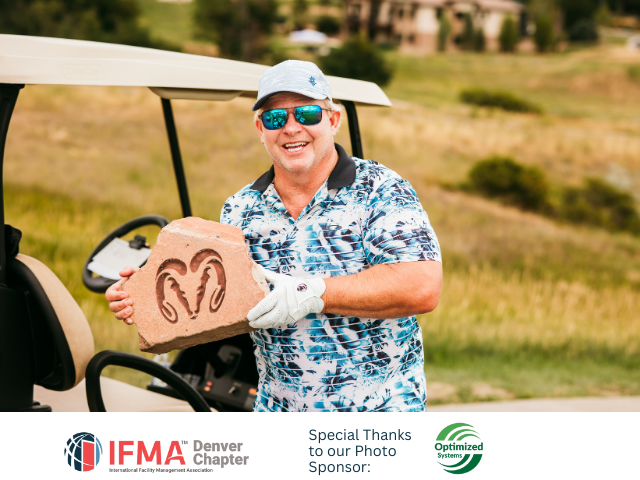 Man holding engraved rock, standing near golf cart on course. He is smiling and wearing sunglasses and golf attire.
