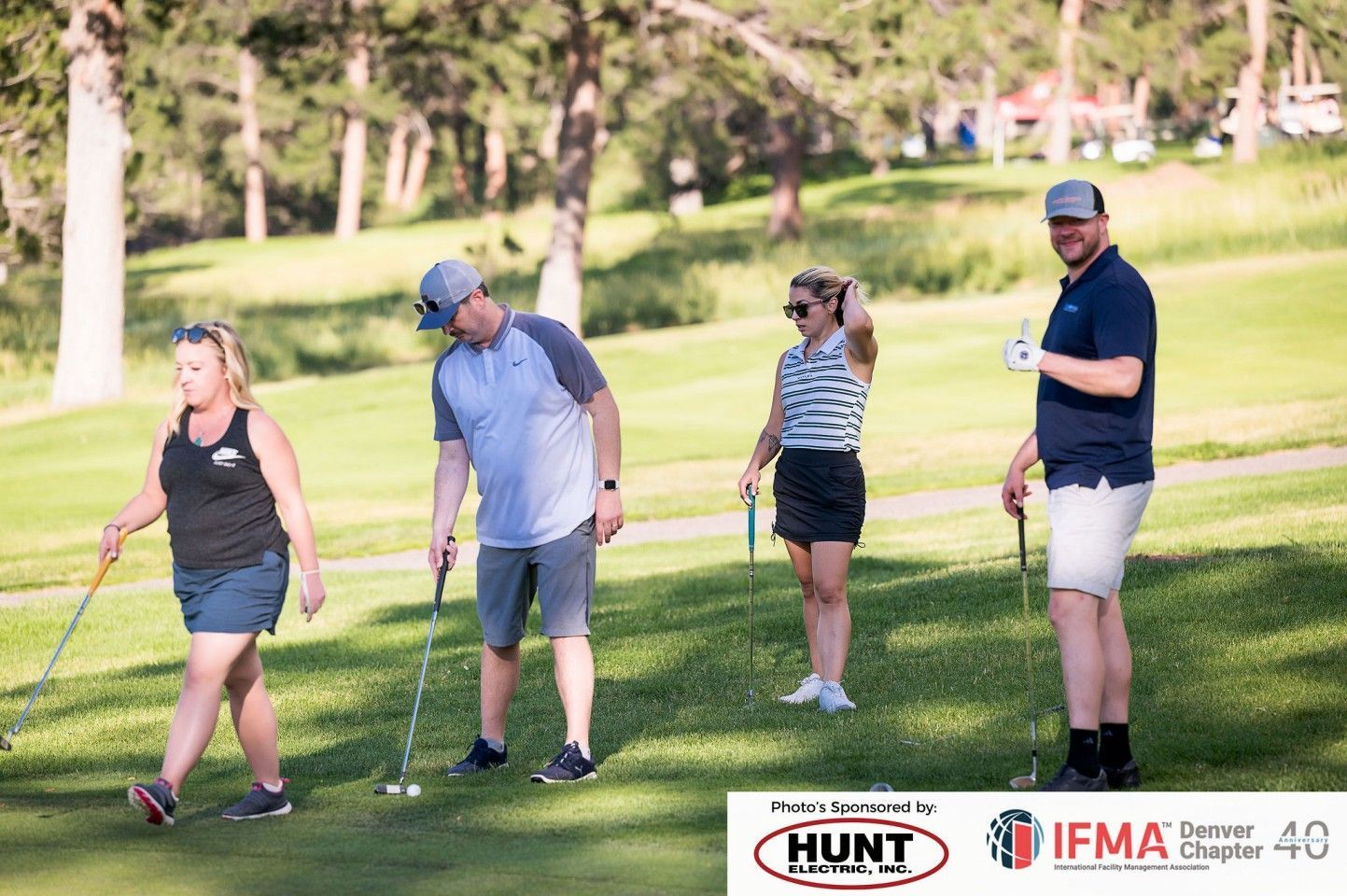 Four people playing golf on a green, sunny day.