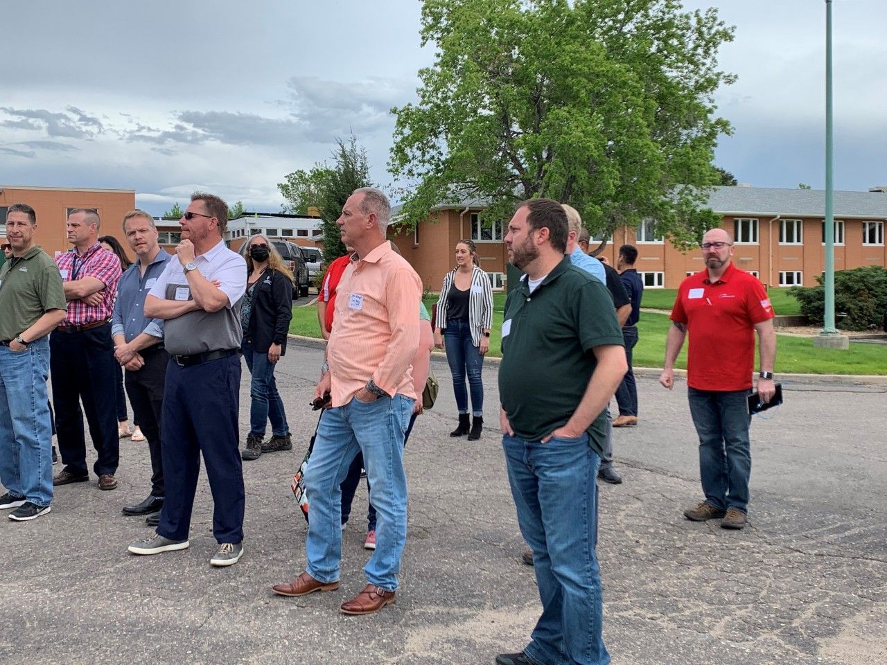 Group of people standing outside, looking upwards. Buildings and cloudy sky in the background.