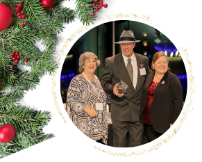 Three people smiling, one holding an award, framed by festive holiday decorations.