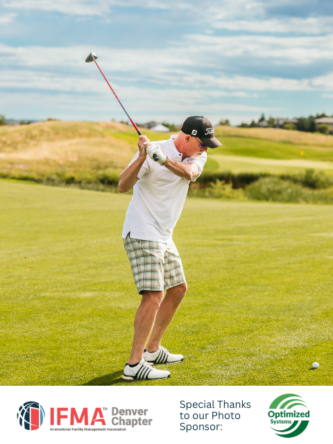 Man in white shirt and plaid shorts swings golf club on a green course.