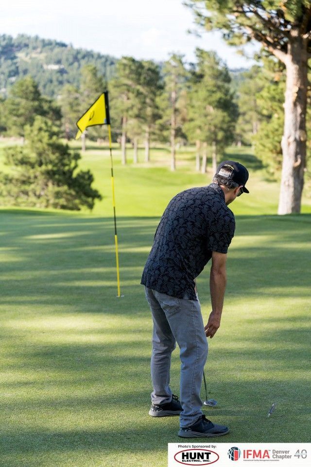 Golfer about to putt on a green. Yellow flag, trees, and mountains in the background.