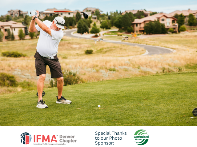 Man swinging golf club on green, with houses and path in background.
