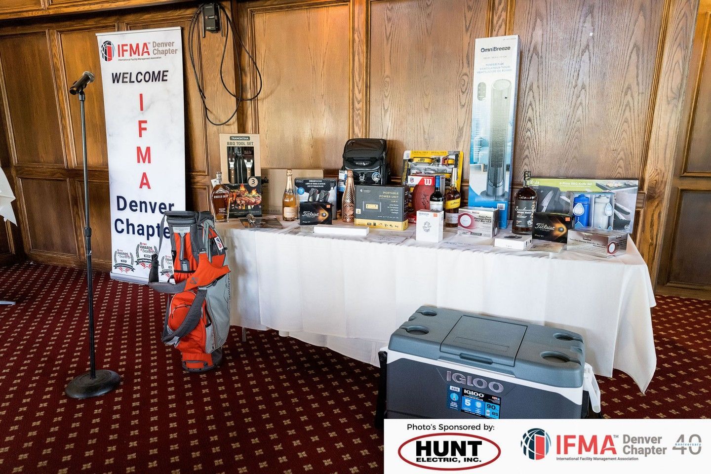 A table with items, including a golf bag, cooler, and various gifts, at an IFMA Denver Chapter event.
