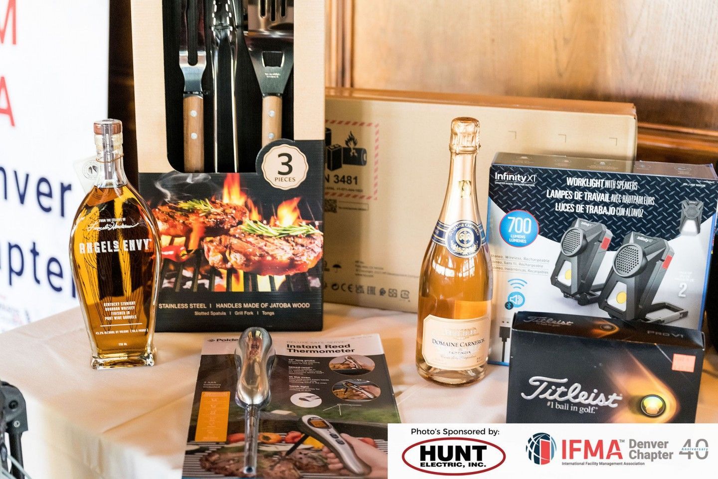 Gift basket with alcohol, grilling tools, and Titleist golf balls on a table.