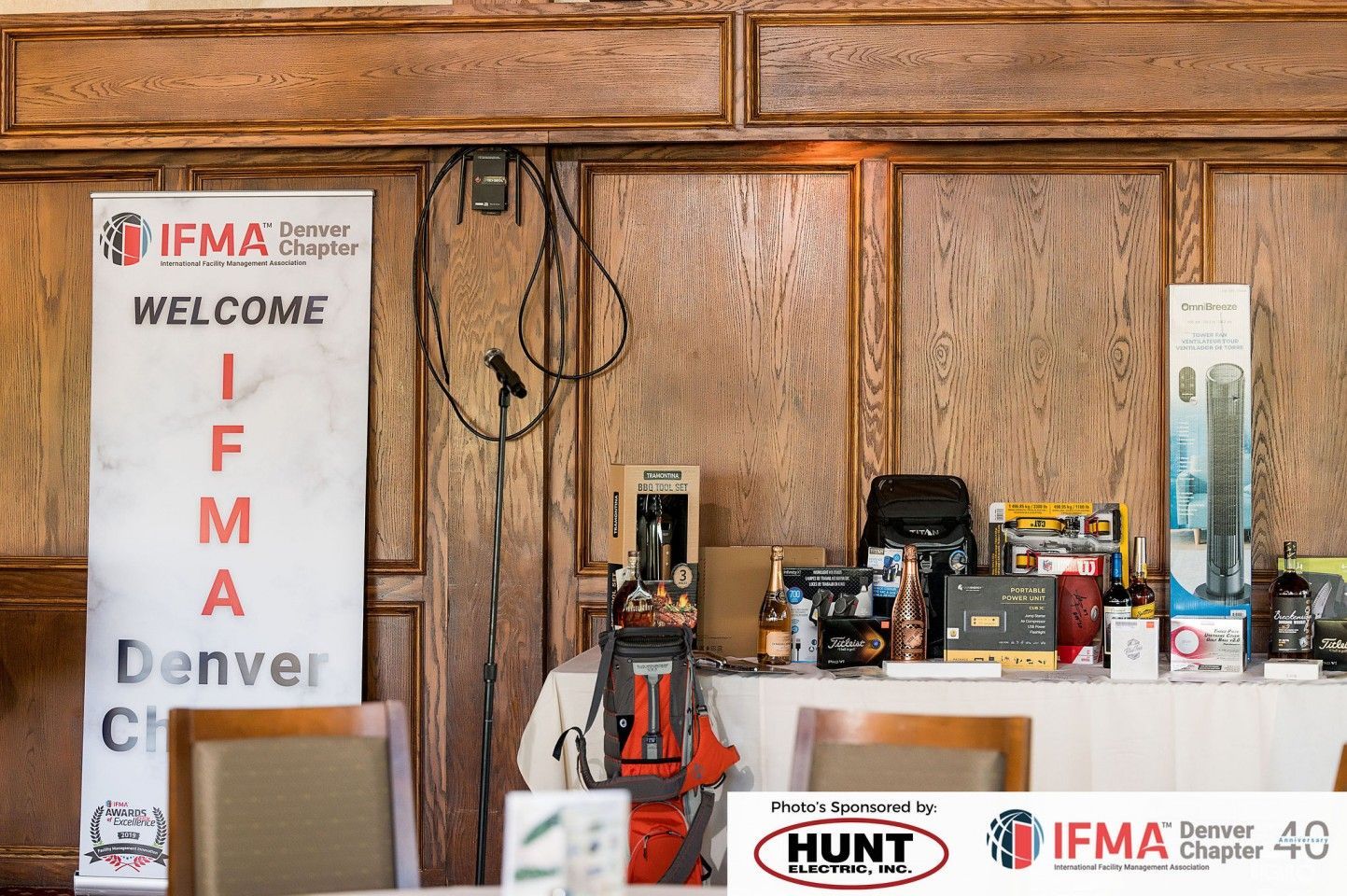 IFMA Denver Chapter event, welcome banner, prizes on table, wooden paneling background.