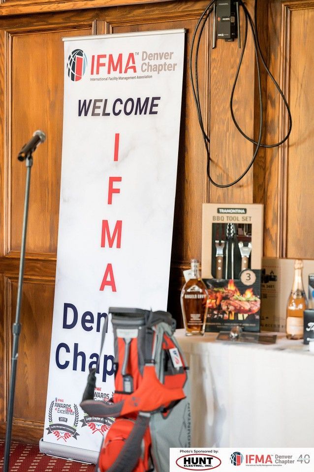Banner for IFMA Denver Chapter with microphone, gifts, and a golf bag.
