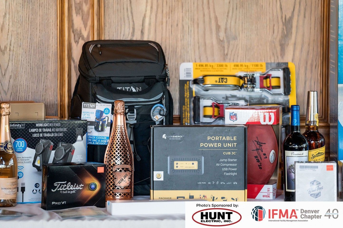 Assortment of prizes including a backpack, champagne, power unit, football, and alcohol on a table with sponsor logos.