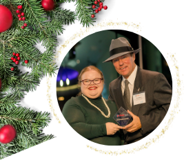 Woman in green top and man in hat holding an award next to Christmas decorations.