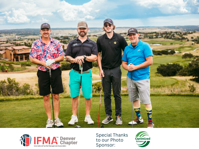 Four men on a golf course posing. Green field, blue sky, and a scenic background.