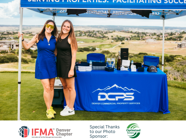 Two women stand at a table with DCPS logo, smiling. They're at an outdoor event with a golf course view.