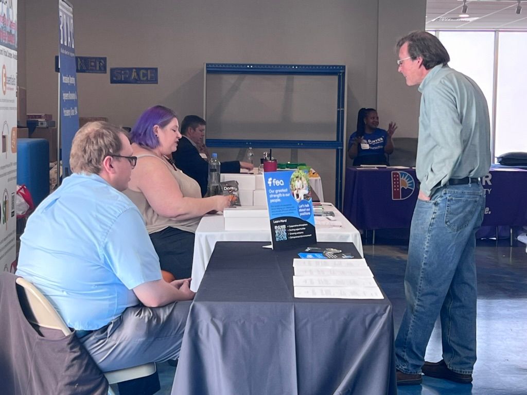 People at a table, discussing. One person stands, speaking to two seated people. Event setting.