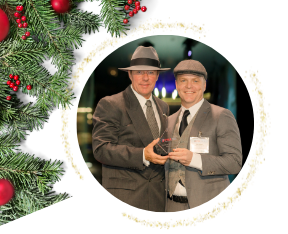 Two men in suits holding an award, with Christmas decorations on the left and around the photo.